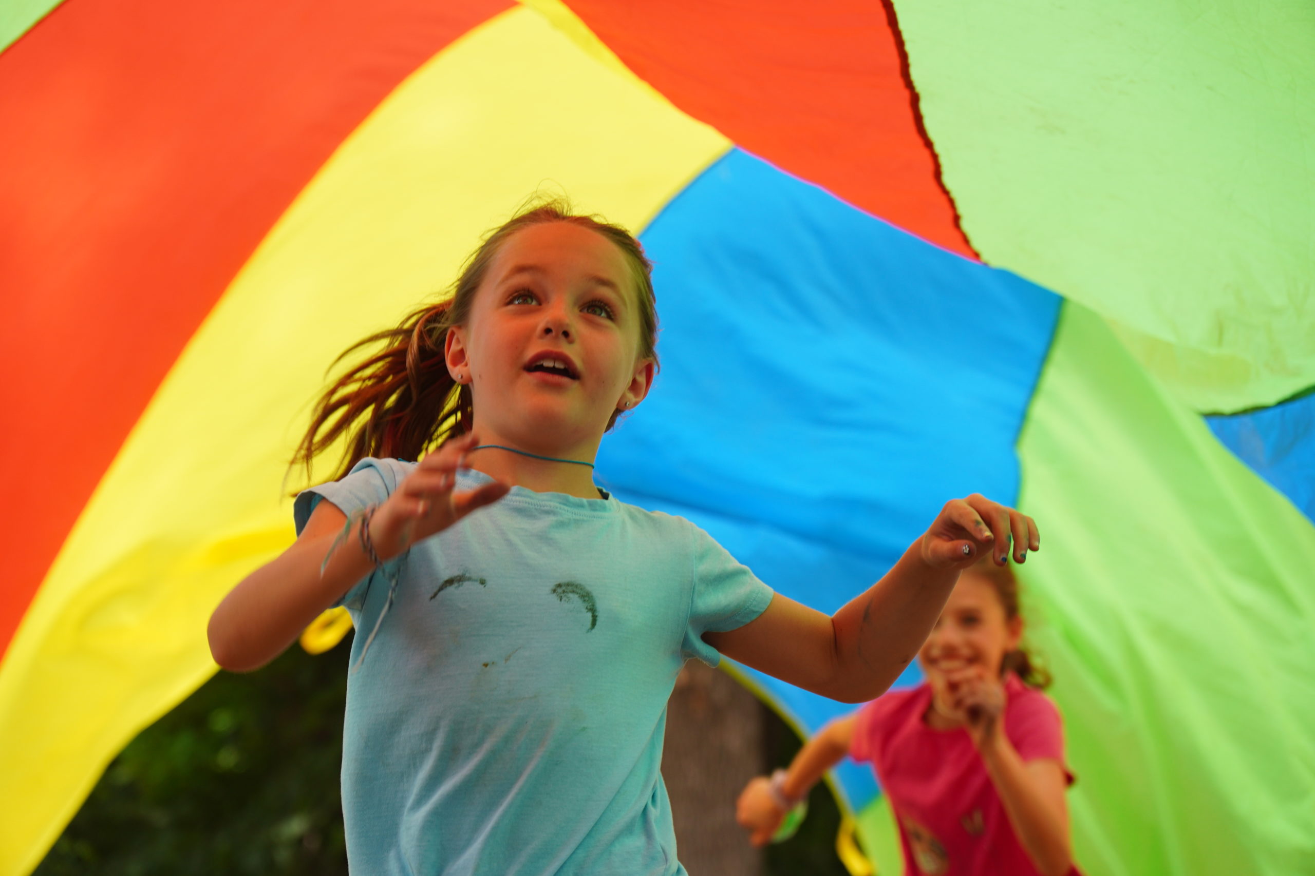 To children joyously running under a brightly colored parachute.