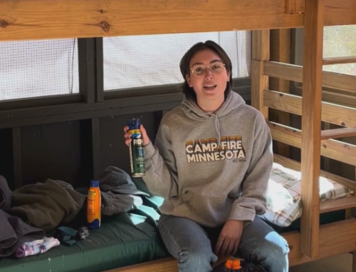 camp staff member holding up a can of bug spray will sitting on a cabin bunkbed
